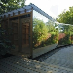 Multipurpose summerhouse in the UK functioning as an artist's studio, garden shed. The 8-meter mirror foil reflects the foliage and helps the structure disappear into the landscape. By Ullmayer Sylvester.