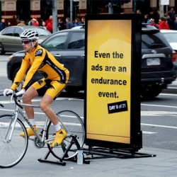 An advertisement for SBS's coverage of the Tour De France that is an epic 21 day endurance event for one Melbourne cyclist. His pedaling is powering a scrolling metrolite from 8-4, stopping only for two rest days as per the actual event.