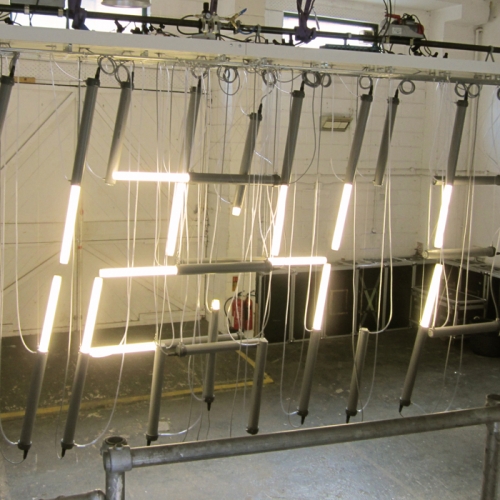 The Tube Lamp Clock by Lambert Kamps is an installation of 30 pneumatically moving Tube Lamps installed and steered as a digital clock. The amount of light can be controlled by moving the light emitting tube in or out the outer tube by compressed air.