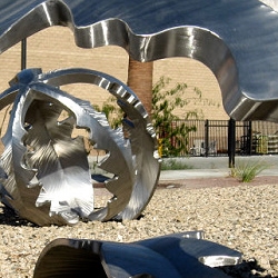 A giant pun in metal, "Tumbling Weed" is a stainless steel sculpture by artist Heath Satow. The five leaves of each "weed" appear as a head, two arms, and two legs, like a child doing a somersault.