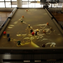 The CueLight uses a conventional pool table as it’s canvas and the paint brush is an overhead projector equipped with sensors and motion detectors. The projector creates images on the pool table based on how the game is played